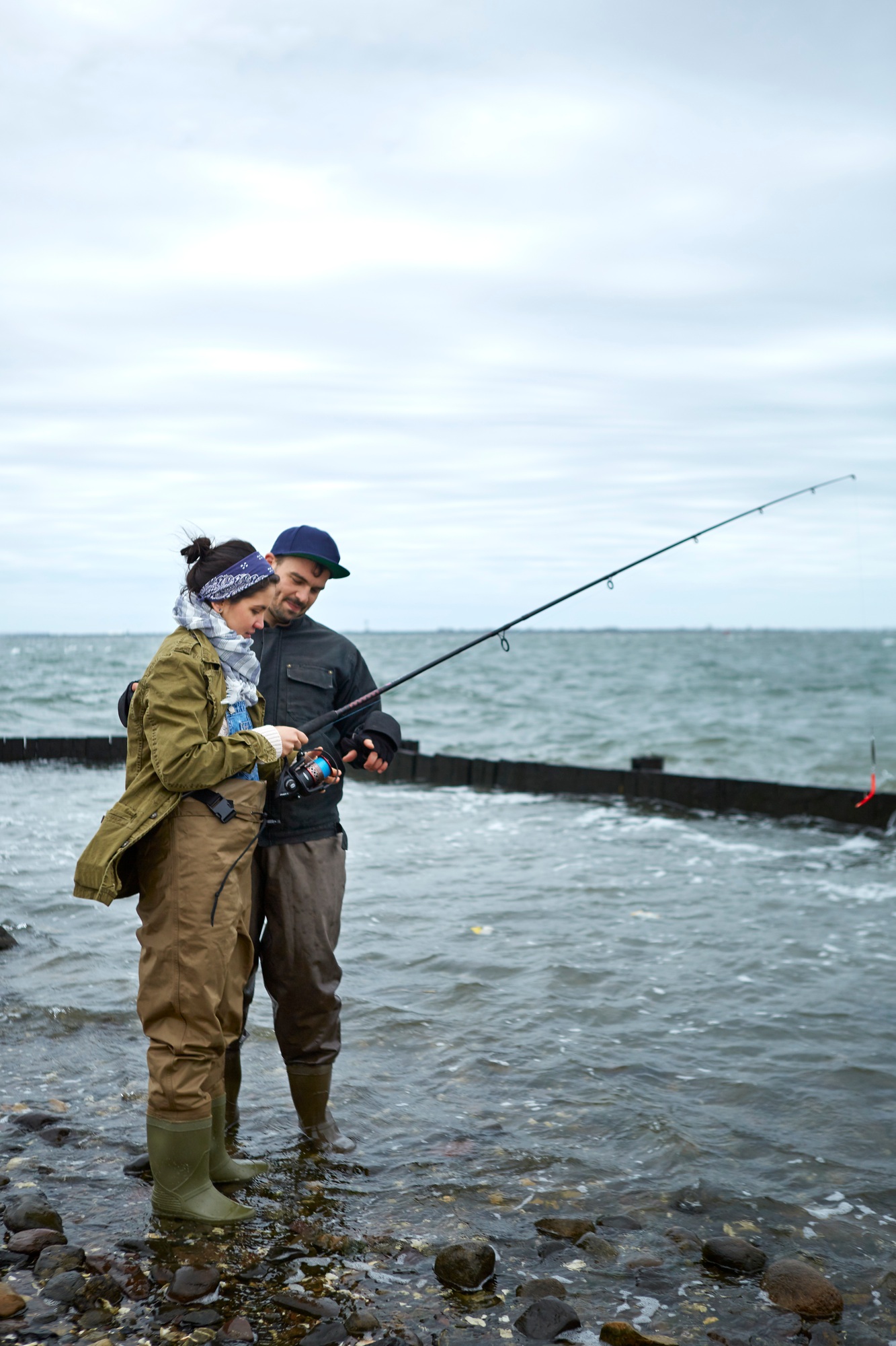 Young man ankle deep in water teaching girlfriend sea fishing